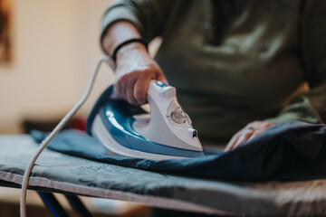A senior woman smooths fabric using a modern electric steam iron on an ironing board, emphasizing...