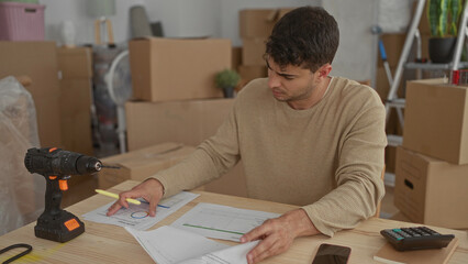 Man taps phone and reviews files in home as hispanic young male amid moving boxes and documents.