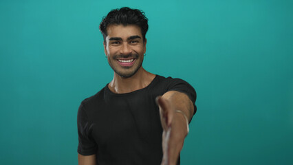 Man smiling warmly extends hand for handshake in teal studio set; welcome connection trust...