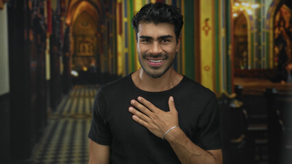 Smiling hispanic man with a friendly expression placing hand on chest in ornate hotel building...