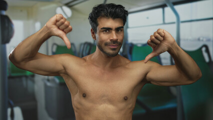 Shirtless hispanic young man bares chest with thumbs down on bus interior seat in street;...