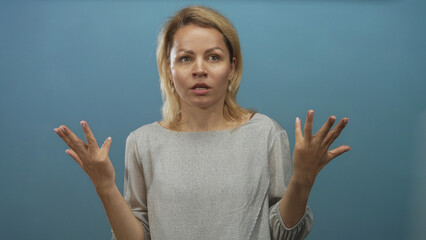 Young blonde woman performs a casual shrug gesture with both bare palms raised in a soft blue...