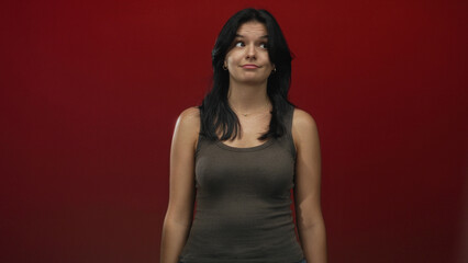 Young hispanic woman with bare shoulders wearing a brown tank top looking upward in a red studio;...