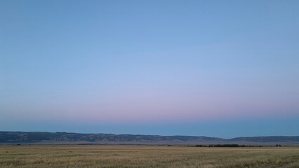Fototapeta premium Pastoral landscape with vast field and distant mountains under a serene twilight sky creating a sense of peaceful solitude