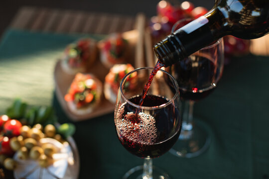 Red wine being poured into a glass on a terrace table with delicious gourmet appetizers in summer