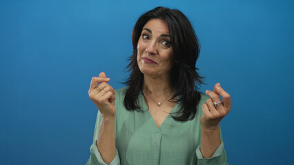 Hispanic middle age woman smiling and making money gesture with hands in a blue studio setting;...