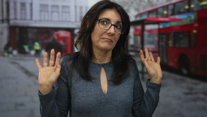 Middle aged hispanic woman wearing glasses and a blue sweater holding up hands in busy urban...