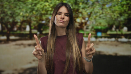 Hispanic woman expresses disagreement with gestures in a sunny park setting, surrounded by lush...