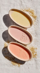 Fototapeta premium Three Oval Dishes with Colorful Liquids and Brown Sugar on White Linen for a Spa Treatment