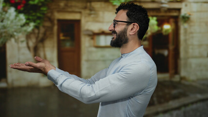 Hispanic man with beard smiling outdoors on a street presenting something interesting with open...