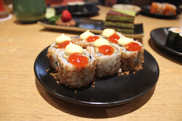 Close-up of Fusion Sushi Rolls Topped with Mayonnaise and Sauce on a Black Plate