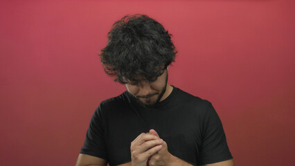 Young man with beard in front of a vibrant red background expressing serene contemplation with...