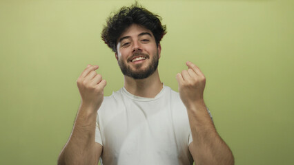 Young hispanic man with beard makes a heart gesture with his fingers against a vibrant yellow...