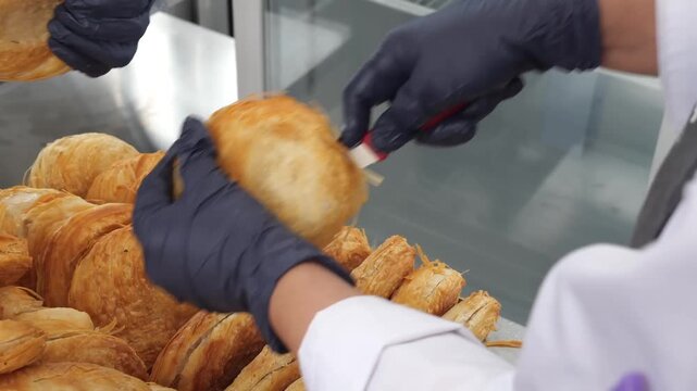 A person uses a tool to cut open crispy, golden-brown pastry shells, creating a pocket for filling. Other chefs take these pastries and stuff them with various ingredients.