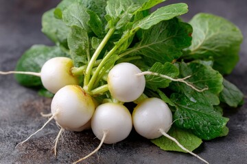 Fresh white radishes with green leaves displayed on a dark textured surface in a kitchen setting