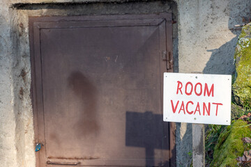 A white sign displaying 'Room Vacant' placed near a locked metal door