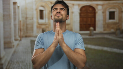 Young hispanic man expressing gratitude at an old university courtyard outdoors, with a serene...