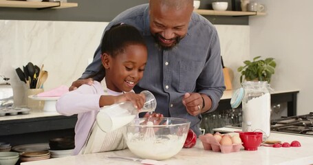 African American father guiding daughter whisking batter in bowl on kitchen island for baking - Powered by Adobe