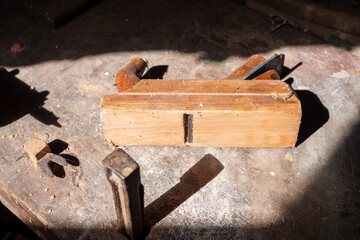 Old wooden hand plane on a worn workbench in a rustic workshop. Traditional carpentry tool used for smoothing wood, showing signs of age and long-time use.