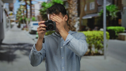 Young hispanic man with camera on city street showcasing excitement and focus outdoors in a vibrant...