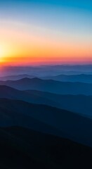 Fototapeta premium Blue mountain range at sunset with orange sky and distant peaks image