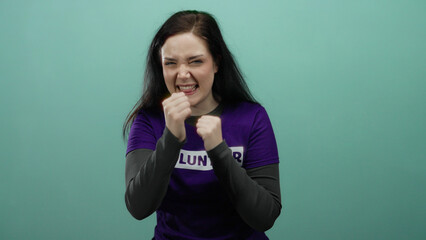 Woman with brunette hair in purple volunteer shirt playfully posing with fists in front of green...