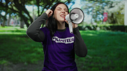 Woman with megaphone passionately speaking in a park outdoors during a volunteer event.