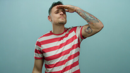 Hispanic male looking intently into the distance, standing against a solid blue background,...