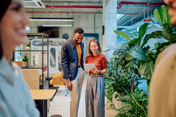 Two smiling business partners collaborating on a digital tablet in a modern green office filled with plants and innovative design elements