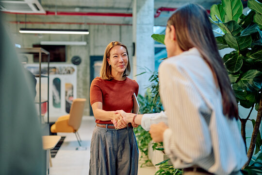 Two happy businesswomen shaking hands in modern office after reaching successful agreement, concept of cooperation and partnership - Powered by Adobe