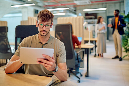 Employee concentrating on his tablet in a bustling office environment, showcasing workplace productivity and technology integration