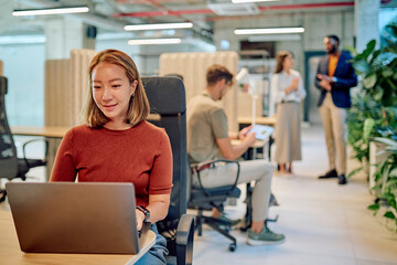 Focused employee using laptop in busy office environment, demonstrating productivity and concentration in a collaborative workspace