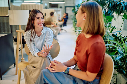 Two businesswomen are sitting in chairs and having a friendly conversation in a bright, modern office environment