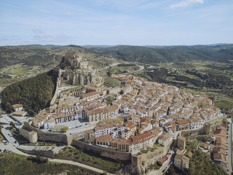 Fototapeta Aerial view of the ancient walled city with its red-tiled roofs and imposing castle perched atop a hill, bathed in warm sunlight, Morella, Valencian Community, Spain.