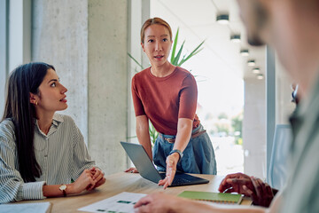 Asian businesswoman leading a meeting with her colleagues, presenting a project on a laptop in a...