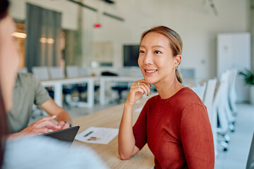 Asian businesswoman attending a meeting with colleagues in a modern office, using a tablet and...