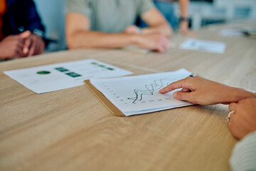 Businesswoman analyzing a financial chart while discussing strategies with colleagues during a meeting in a corporate office setting