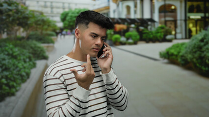 Young man talking on phone in an urban street setting with a blurred city background, conveying communication and lifestyle in an outdoor environment.