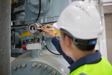 Gas pressure monitoring at industrial substation is performed by technician wearing safety gear to...