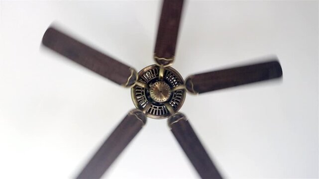 A ceiling fan spinning with visible motion blur on a white ceiling, slow motion