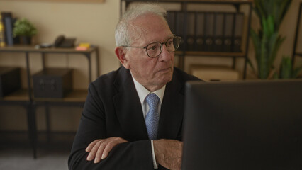 Senior man in a business suit sitting at a desk in an office setting, capturing a professional...