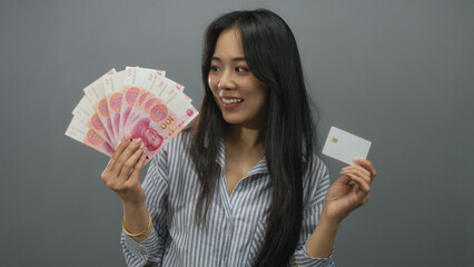 Woman holding chinese yuan banknotes and a credit card against an isolated grey background,...