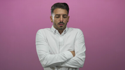 Young hispanic man wearing crisp white shirt crossing arms against a pink studio backdrop;...