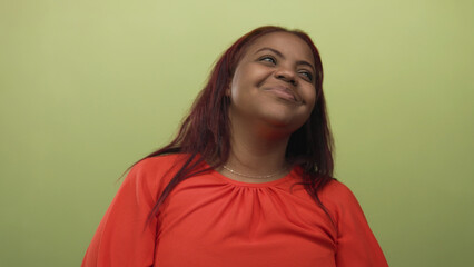 Fototapeta premium Woman in a red blouse tilts head and closes eyes with a gentle smile in a green studio; calm introspection serenity.