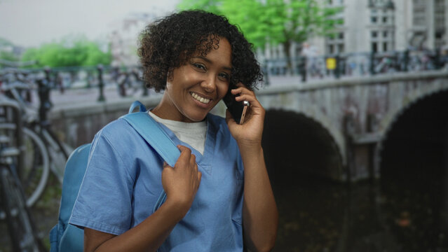 Woman smiling walks on street carrying backpack and holds smartphone to ear; joyful connection journey.