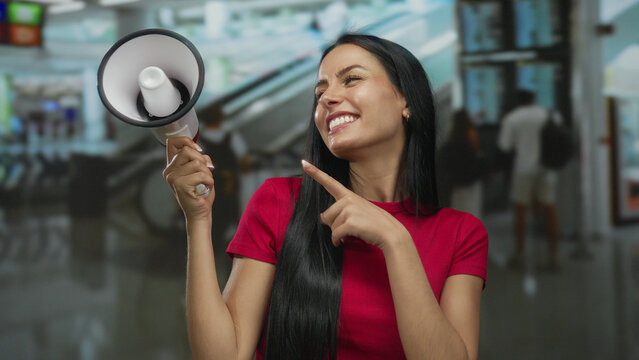 Smiling hispanic woman holding megaphone in vibrant airport terminal setting creates lively announcement atmosphere.