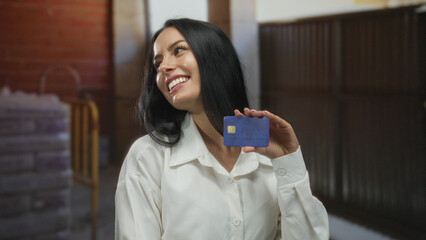 Woman smiling at construction site indoors pointing to herself while holding a blue credit card...