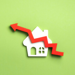A white house model with a red zigzag upward arrow, symbolizing rising property value on a green...