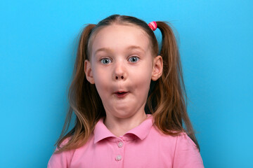 Funny close-up of a young girl in a pink shirt making a surprised expression against a bright blue background.