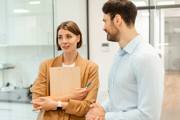 Businesswoman holding clipboard talking with businessman in office